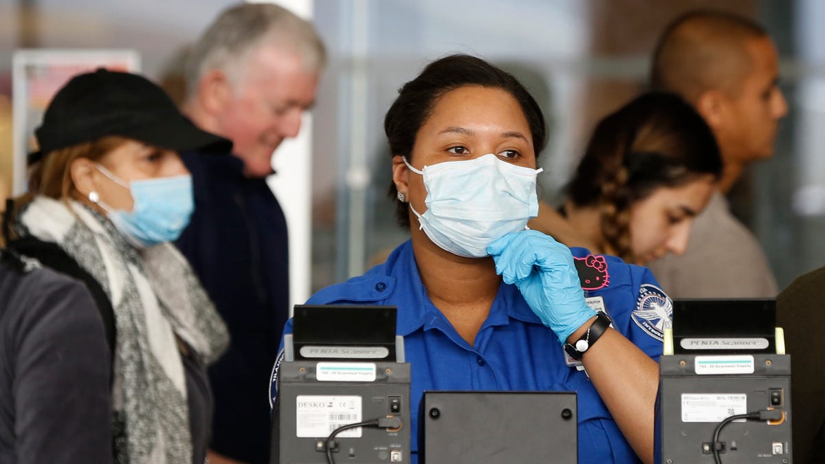 A Transportation Security Administration (TSA) employee adjusts her face mask while screening passengers entering through a checkpoint at John F. Kennedy International Airport, Saturday, March 14, 2020, in New York.