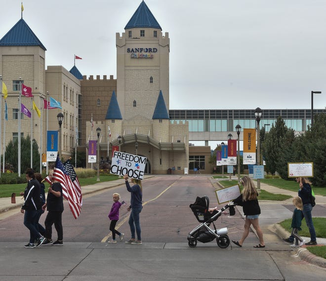 People march in front of the Sanford Children’s Hospital on their way to the main Sanford Hospital on Tuesday, September 14, 2021. People gathered to protest the COVID-19 vaccine mandate Sanford Hospital has put in place for its employees.