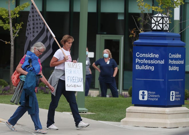 A couple of protesters walk past masked workers on their way to take part in a protest on September 15 against vaccine mandates against Akron Children's Hospital.  The hospital puts an undisclosed number of employees who have not received a required COVID-19 vaccine on unpaid leave.