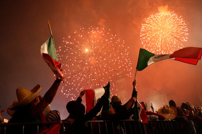 Revelers wave Mexican flags as fireworks explode after President Andres Manuel Lopez Obrador gave the annual independence shout from the balcony of the National Palace to kick off Independence Day celebrations, in Mexico City, Sunday, Sept. 15, 2019.