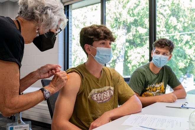 Benzie-Leelanau District Health Department retired women's health nurse practitioner Jan Frazee gives first dose of the Pfizer Covid-19 vaccine to Dashel Courson (center), 15, of Northport as his brother Lantz Courson, 13, looks on during a community vaccination event at Northport Public School in Northport on September 16, 2021.