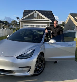 The author standing besides his Tesla which he charges via the solar panels on his home's roof.