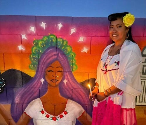 Anitra "Yukue" Molina poses next to her mural with a candle illuminating the wall.