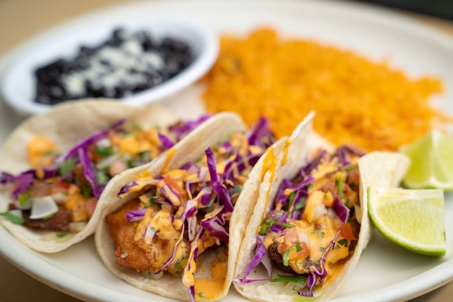 Baja Fish Tacos are a seafood special at Fiesta Mexican Restaurant with three fried tilapia tacos on a soft corn tortilla, topped with red cabbage, pico de gallo, and chipotle sauce, served with Mexican rice and black beans.