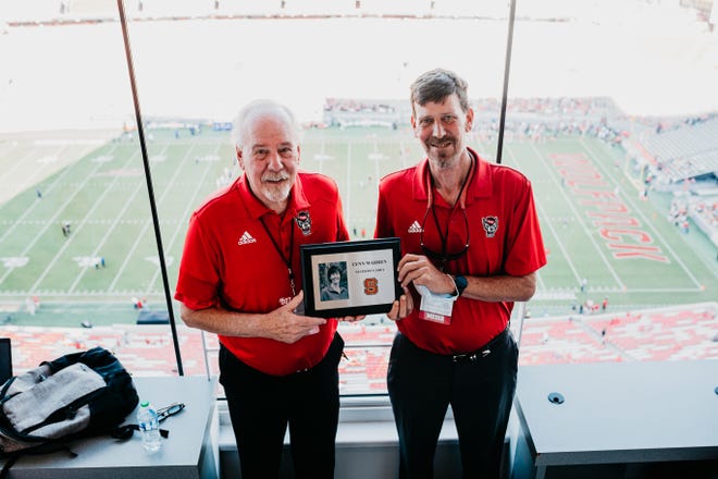 Mike (left) and Randy Warren pose with a picture of their sister, Lynn, before Saturday's game against Louisiana Tech. Their father, Roger Warren, began keeping stats for Wolfpack football games over 50 years ago, but since his retirement in 2019, his kids have kept that responsibility in the family.