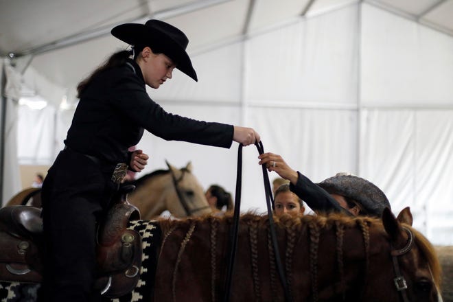 Caraline Higgins grabs the reins of Chick from her coach Kelsey Ebke before her Junior Varsity Novice Ranch Riding class in the Taft Coliseum on Thursday.