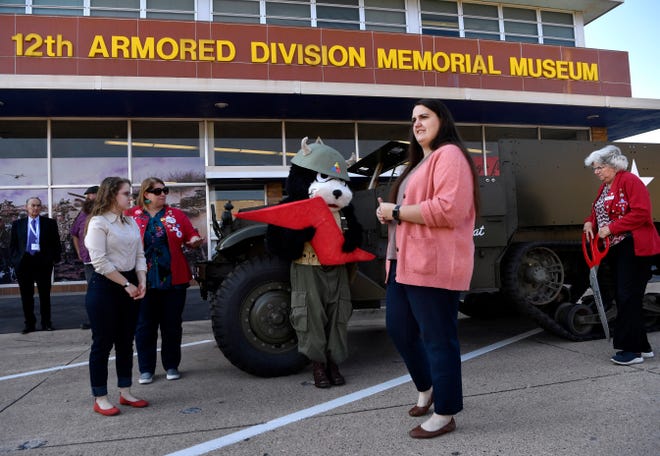 Mikayla Ballew, the executive director of the 12th Armored Division Memorial Museum (in pink), stands before one of the museum's pieces nicknamed "The Alley Cat", a 1943 White M-3 halftrack, Wednesday. The museum celebrates 20 years Saturday.