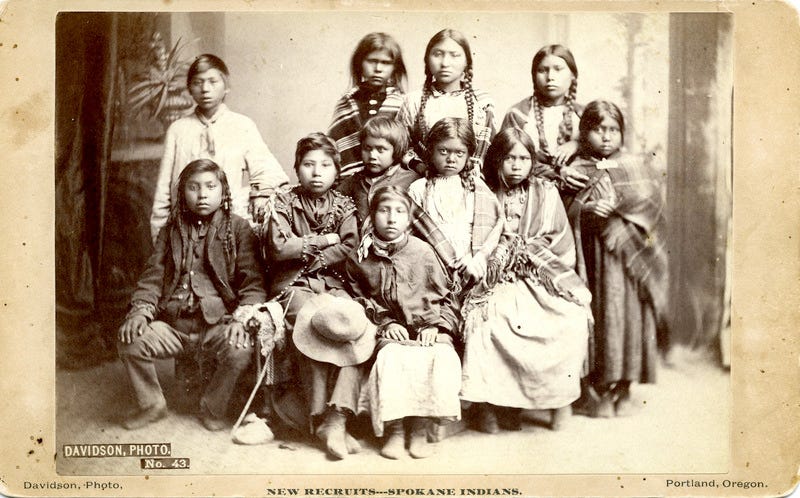 The second group of Spokane students taken from the band of Chief Lot as photographed July 8, 1881 in a Portland studio on the way from their homes to the school. Their names as given on the school roster are: Alice L. Williams; Florence Hayes; Suzette (or Susan) Secup; Julia Jopps; Louise Isaacs; Martha Lot; Eunice Madge James; James George; Ben Secup; Frank Rice; and Garfield Hayes.

► The Forest Grove Indian School Superintendent has this photograph made for fundraising and promotional purposes, according to the Pacific University Archives. It is intended to be a "before" picture, which he pairs with a later "after" picture that was taken when the children had been at the school for seven months.