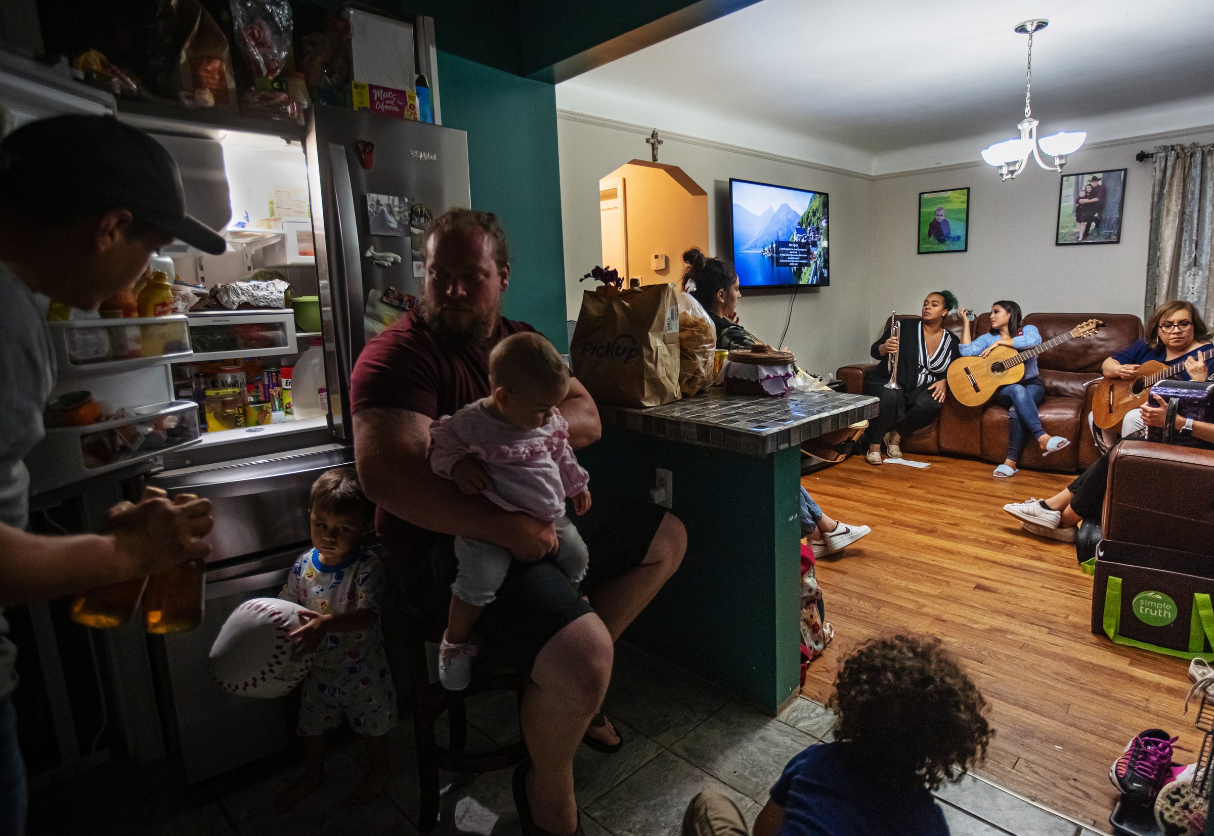 Eloy Barraza, of Lincoln Park, left, gets a couple drinks from the fridge as Jeremy Rowe, of Livonia, holds his daughter Morgan while his son Keegan plays on the floor as their wives take part in a rehearsal for Mariachi Femenil Detroit at Barraza's home in Lincoln Park on Friday, Oct. 1, 2021. Mariachi Femenil Detroit director Camilla Cantu, left, leads members Sherray Rowe, of Livonia, Rita Ramirez, of Lincoln Park, Alida Cazares, of Detroit, and Marian Vanne, of Auburn Hills, while going over a song the day before playing at a wedding in Detroit.