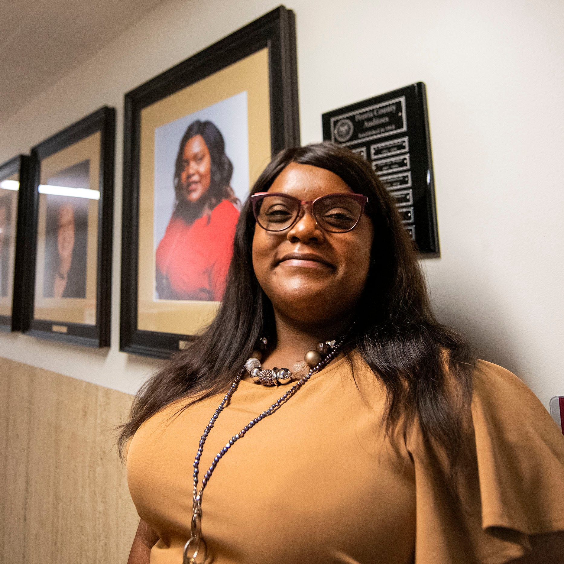 Peoria County Auditor Jessica Thomas stands by a row of portraits of county auditors outside of her office in the Peoria County Courthouse. Proposed budget cuts by the Peoria County Board could remove her three staff members.