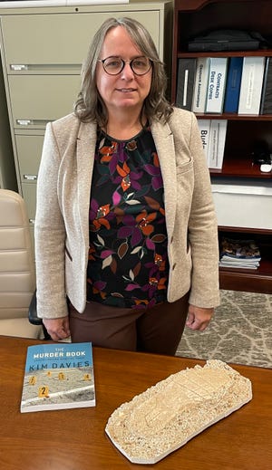 Dr. Kim Davies, dean of Augusta University’s Pamplin College of Arts, Humanities and Social Sciences, stands with her new book in the subject of murder, and a plaster cast of a footprint given to her by a former student who interned with the Georgia Bureau of Investigation.