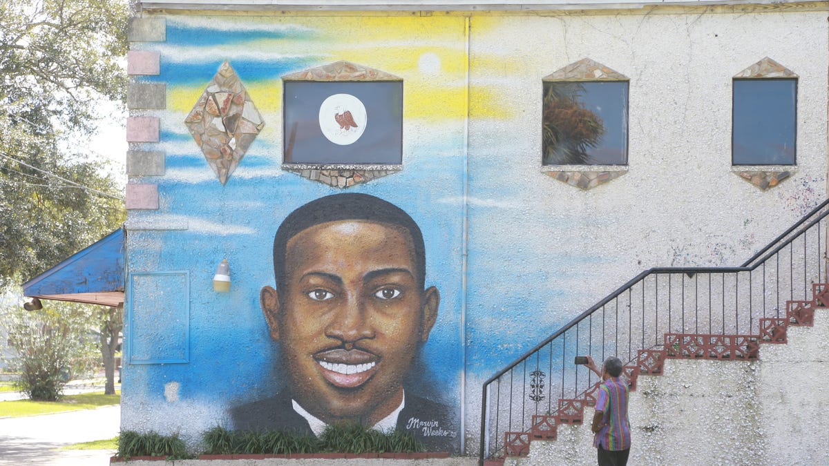A man uses his phone to record the Ahmaud Arbery mural on the side of the Brunswick African American Cultural Center.