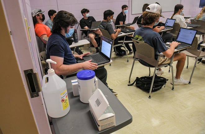 Clemson student Kaleb Knecht looks at his laptop near a table of hand sanitizer, masks, and wipes,  in an English business writing, in Clemson, S.C., October 21, 2021.