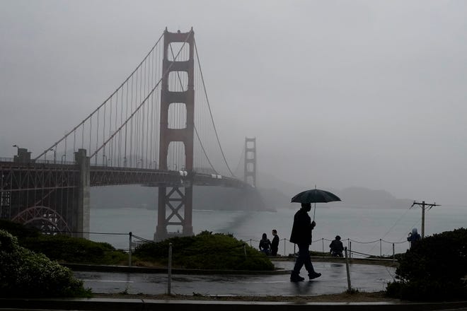 A pedestrian carries an umbrella while walking on a path in front of the Golden Gate Bridge in San Francisco.