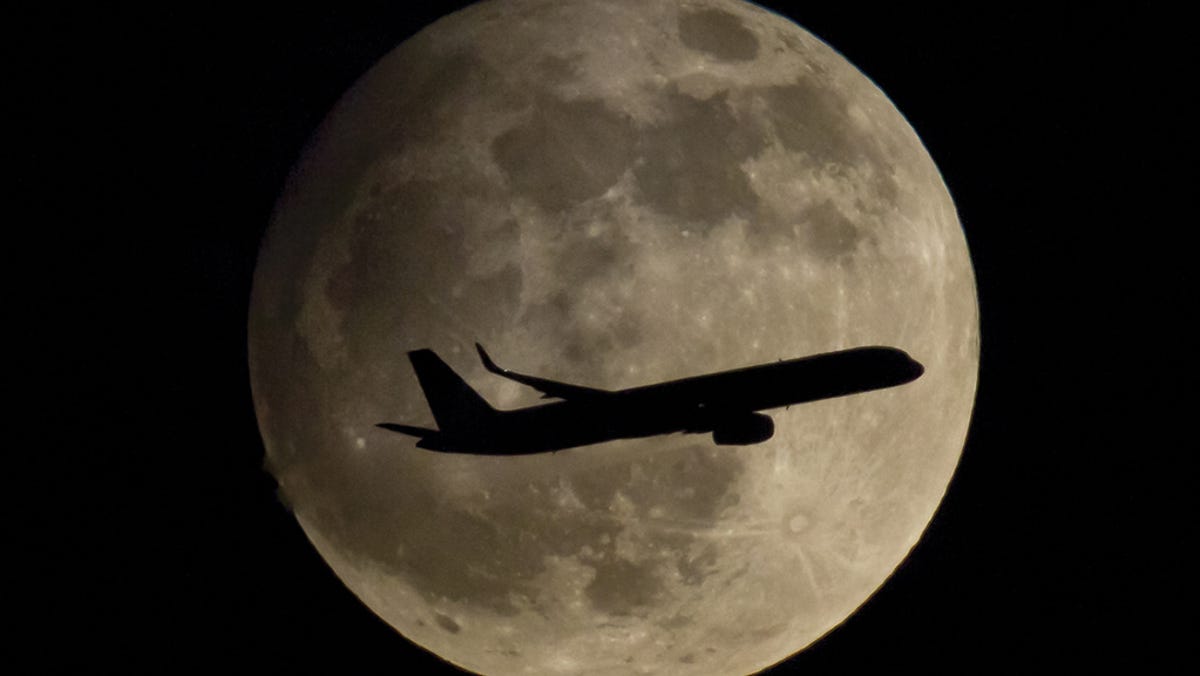 In this picture made available Friday, April 26, 2013, a passenger airplane is about to land at the airport in Frankfurt, Germany, thereby passing the moon which is clearly visible at night.