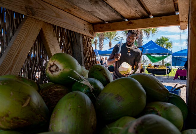 Jacques Belony cuts coconuts at his Taino Tiki stand at the Riviera Beach Greenmarket in Riviera Beach on October 31, 2021.