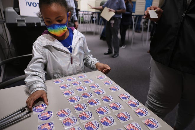Five-year-old Savannah Angel Harris picks up a sticker reading "Future Voter" while accompanying her mother to vote at the Fairfax County Government Center on Tuesday. Virginians are voting in a gubernatorial race that pits businessman, Republican candidate Glenn Youngkin against Democratic gubernatorial candidate, former Virginia Gov. Terry McAuliffe.
