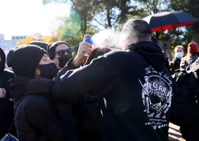 A counterprotester, center left, releases a chemical irritant on a protester who came to attend a Super Happy Fun America and the Refounding Fathers Coalition called "Rise Against Tyranny Rally," Sunday, Nov. 7, 2021, as a scuffle breaks out between the two factions on the Boston Common in Boston. The counterprotesters and demonstrators, opposing mask and vaccine mandates, clashed Sunday, leading to two arrests. (Jessica Rinaldi/The Boston Globe via AP)