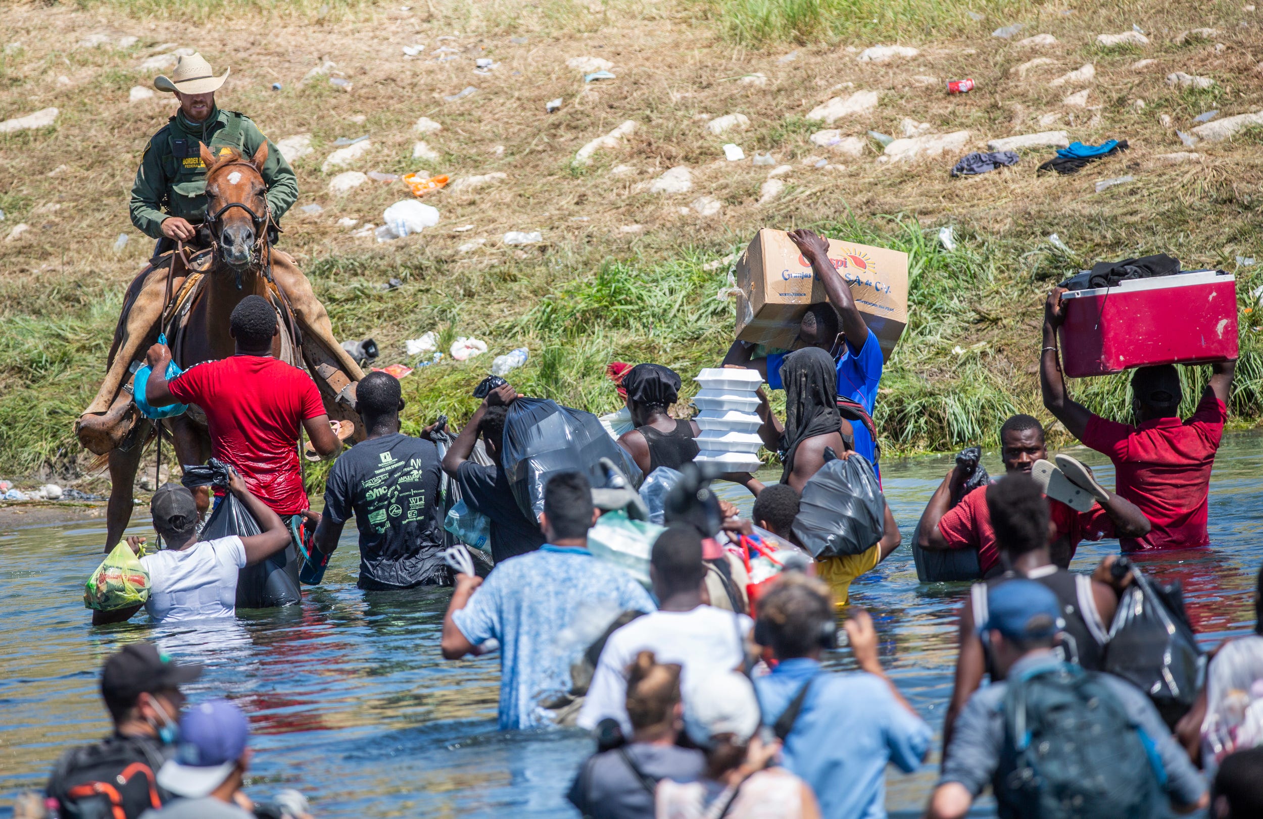 Haitians cool from the heat on the north bank of the Rio Grande in Del Rio, Texas, as a mounted Border Patrol agent approaches on horseback. Minutes later, confrontation ensued after a border tried to prevent other Haitian migrants from returning to the migrant encampment in September 2021.