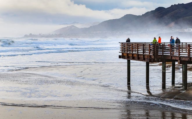 A group of people gather to watch the storm surge from high tides and big surf in the morning in Pismo Beach, California, in January 2016.