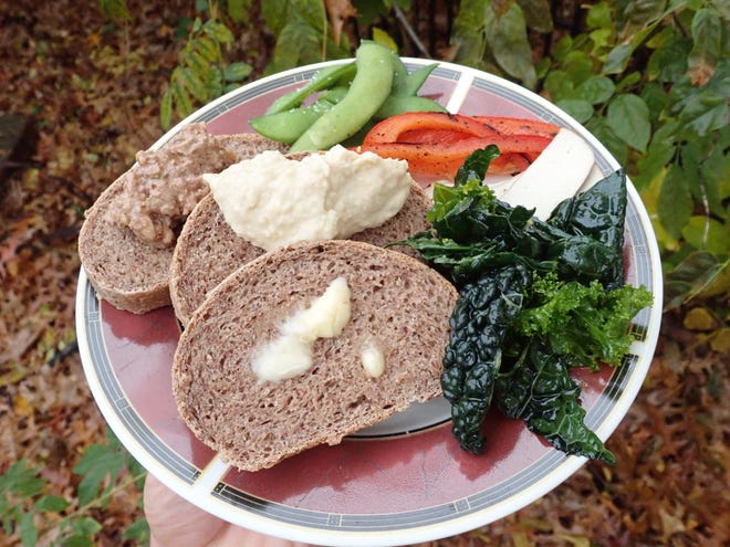 Bread and bread with spreads — vegan butter melting in the front slice, creamy hummus piled onto the second slice and the tapenade heaped onto the back slice; served with fresh vegetables and baked tofu.