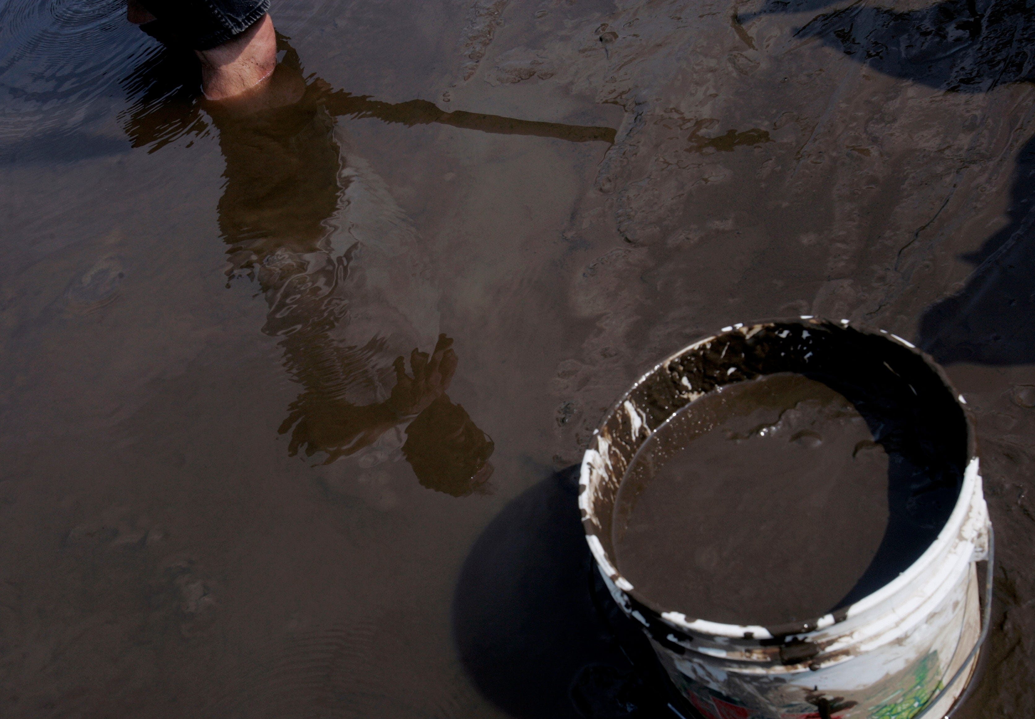 Jim Bintliff is reflected in the murky water while shoveling mud from a small creek in southern New Jersey in 2005. For more than 50 years, Bintliff's Lena Blackburne Baseball Rubbing Mud company has provided high-quality mud to Major League Baseball to get slick, shiny new baseballs ready for play. (AP file photo/Coke Whitworth)