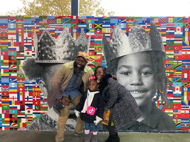 Photographer Erik James Montgomery and Principal Fatihah Abdur-Rahman pose with Ah'Malia Purnell in front of a mural with her likeness.
