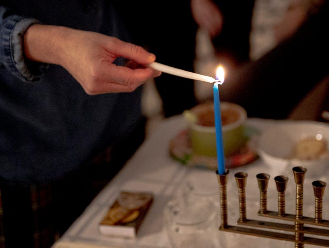 Laura Sawicki uses the shamash to light the first candle on the menorah during an annual Hanukkah dinner party.