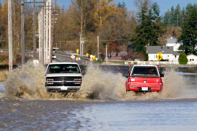 Pickup trucks fill with muddy water as they pass through a flooded road, Tuesday, November 16, 2021, near Everson, Wash.