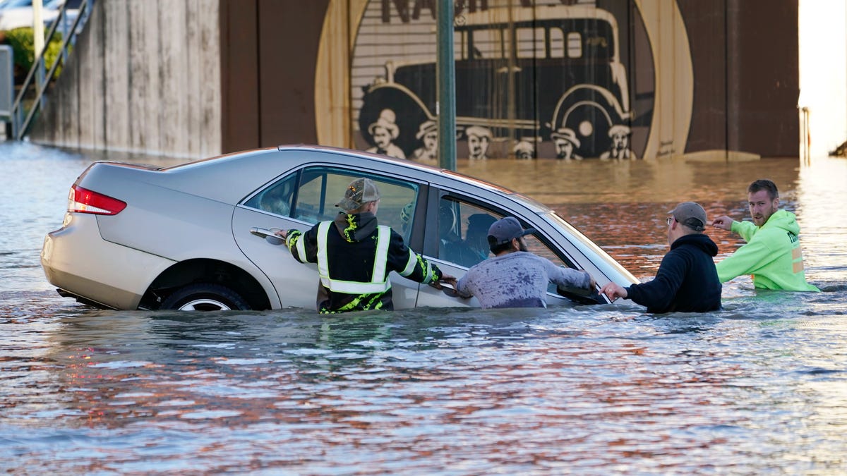 Passersby surround a car whose driver went past a barricade and into the flooded Nooksack River, Tuesday, Nov. 16, 2021, in Ferndale, Wash. About a half-dozen citizens went into the river, where they stopped the car from floating further and muscled it back onshore. No one was injured.