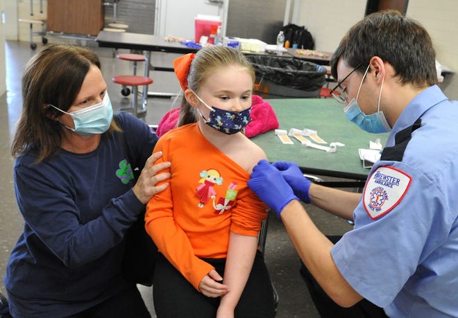Megan Symonds, 7, of Weymouth, center, receives her COVID-19 vaccine from Brewster Ambulance EMT Fran Soljacic, right, as Megan's mom, Danielle Symonds, left, provides moral support during the vaccination clinic at Weymouth High School on Saturday, Nov. 20, 2021.