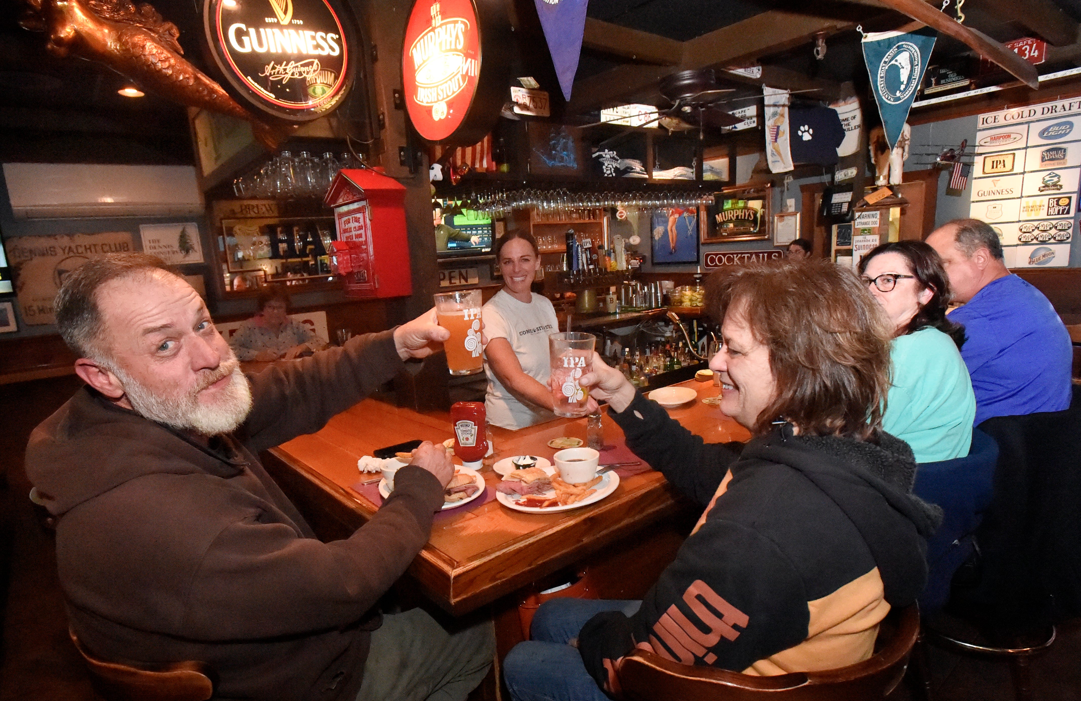 Group of people at the bar raising their beer glasses in a toast to the camera