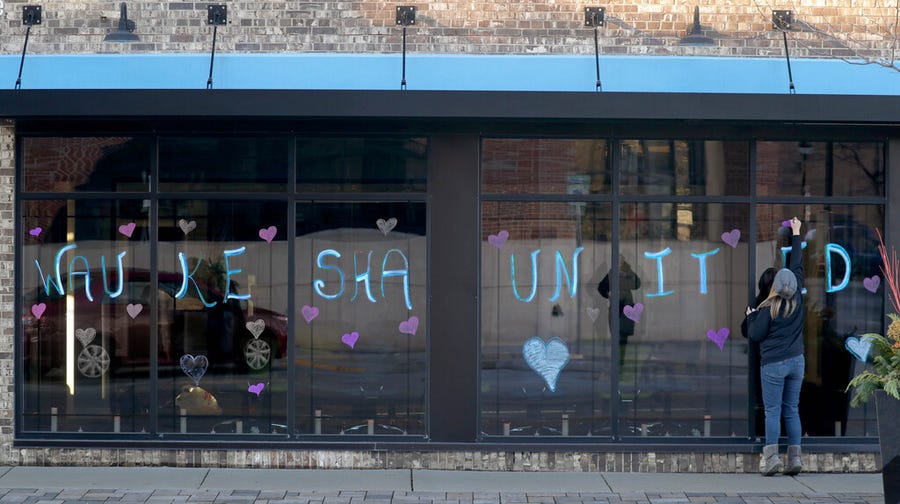 Catie Bauer with Smart Asset Realty finishes off writing Waukesha United outside the business on Main Street at the scene of the deadly Waukesha parade tragedy in Waukesha on Monday, Nov. 22, 2021.