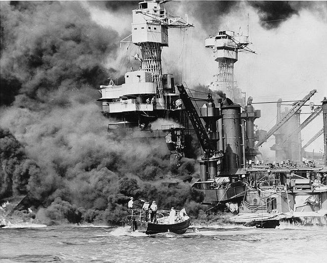 Pearl Harbor, Hawaii. A small boat rescues a seaman from the 31,800 ton USS West Virginia burning in the foreground. Smoke rolling out amidships shows where the most extensive damage occurred. Note the two men in the superstructure. The USS Tennessee is inboard.
