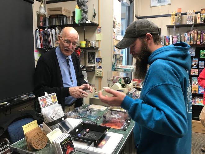 Ken Peczkowski, left, watches as Luke Freeman rolls a set of dice to determine his discount at Griffon Bookstore on Saturday, November 27, 2021.