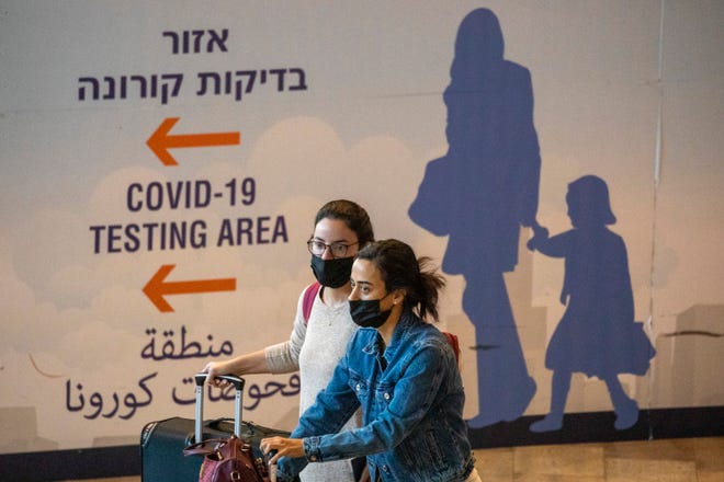 Travelers wearing protective face masks arrive at Ben Gurion Airport near Tel Aviv, Israel, Sunday, Nov. 28, 2021. Israel on Sunday approved barring entry to foreign nationals and the use of controversial technology for contact tracing as part of its efforts to clamp down on a new coronavirus variant. (AP Photo/Ariel Schalit)
