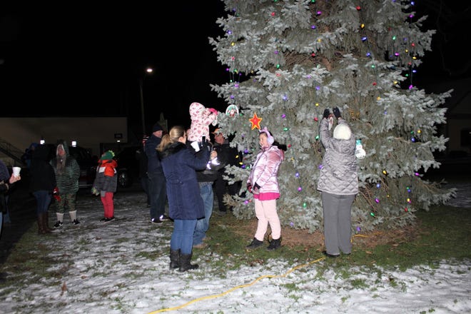 Ida-area residents decorate a 65-foot-tall evergreen tree with handmade ornaments prior to a tree-lighting ceremony Sunday night to kick off the annual Christmas in Ida Festival this weekend. The ceremony was held at dusk in the Ida Township Park behind the fire hall off Lewis Ave. in downtown Ida. The lighting was a tradition that returned during last year’s festival as a “symbol of hope” after a year of the COVID-19 pandemic, said Dale Zorn, executive director of the festival. The lighting took place following the singing of Christmas carols and holiday songs and the serving of doughnuts, roasted marshmallows and hot chocolate. Area families, businesses, community organizations, clubs and school groups were invited to create their own special ornaments for the tree. Anyone who still has an ornament can hang it any time before the start of the festival Friday or it can be dropped off at Zorn’s Service Inc. in Ida, Zorn said.