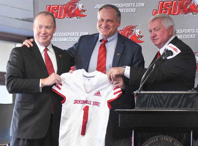 Jacksonville State University President Dr. Don C. Killingsworth Jr., left, and Board of Trustees Chairman Randall Jones, right, hand new head football coach Rich Rodriguez a JSU jersey Tuesday at his introductory news conference.