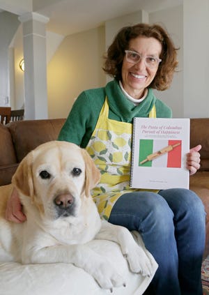 Daniela Di Lorenzo in her New Albany home with the family dog Dolce and the Italian cookbook of her family's favorite recipes. Dolce appears in the book and has tested much of Di Lorenzo's cooking.