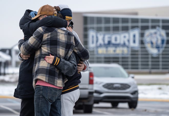 (Left to right) Alexis Lewis of Oxford, Matt McMahon of Hadley, Garrett Latta of Oxford and Mama Ross of Oxford hug while visiting a memorial being built at an entrance to Oxford High School on December 1, 2021, following an active shooter situation at Oxford High School that left four students dead and multiple others with injuries.