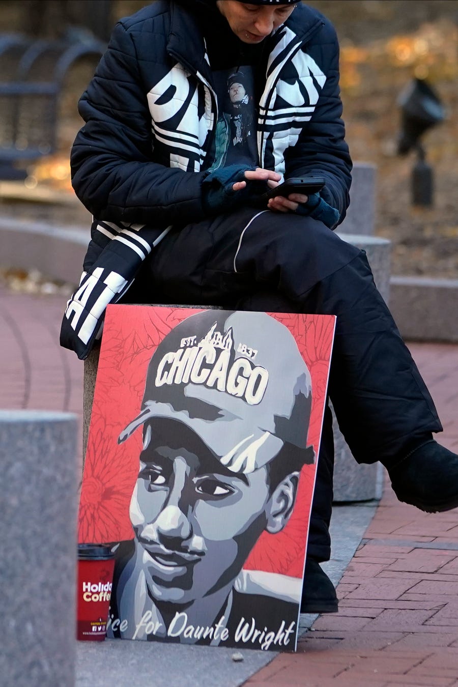 A lone demonstrator sits on a cement barrier with a Daunte Wright poster, Thursday, Dec. 2, 2021, outside the Hennepin County Government Center in Minneapolis as jury selection enters the third day for former suburban Minneapolis police officer Kim Potter.