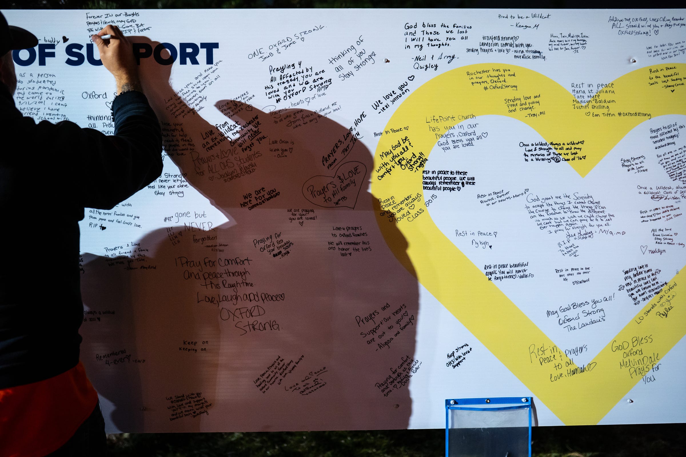 People sign a board with messages of support at a memorial at an entrance to Oxford High School after a vigil in downtown Oxford on Friday, Dec. 3, 2021, for the Oxford community.