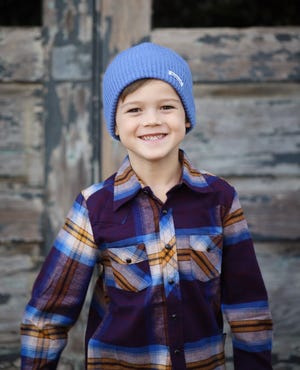 Jaxon Rogers models a blue beanie and plaid shirt sold at Poppy and Harper Boutique.