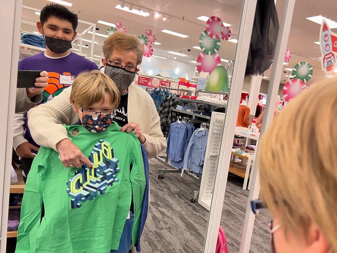 Ten year-old Costa Catholic Academy student David Bailey uses a mirror to check out the look of a green shirt as Carl Sandburg College sophomore Lucas Garcia and volunteer Barbara Klein-Boyer assist during the annual Kiwanis Shopping With the Kids event at Target on Tuesday. [STEVE DAVIS/For The Register-Mail]