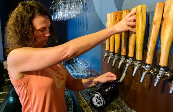 Courtney Murr owner of the Dog Rose Brewing Company in St. Augustine pours some of her company’s beer into a 64-ounce refillable glass growler on Wednesday, Dec. 8, 2021.
