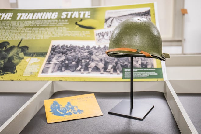 The exhibit includes artifacts such as a brochure loaned by the Tampa Bay History Center about MacDill Field, which was built near Tampa in 1939 and was critical in defending the Gulf of Mexico against Nazi U-boat attacks on merchant ships. To the right is an M1 helmet loaned from Camp Blanding Museum.