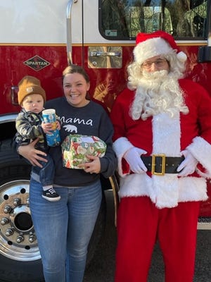 PRINCETON - Christopher Bruning Jr.,  11 months, allows his mother, Jenn Bruning, to hold his gift during his meeting with Santa. Christopher’s father is also a firefighter with the Princeton Fire Department.
