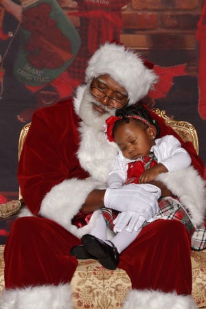 A Santa from Santas Just Like Me snuggles with a child during a photoshoot. Santas Just Like Me provides professional photos with Santas of color for families during the holiday season.