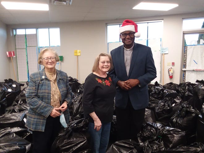 Mary Johnson, Sister Carolyn Capuano, and the Rev. Benson Okpara, pastor at St. Michael Archangel Catholic Church in Plain Township, stand amid a mountain of gifts that parishioners recently donated for the parish's annual Giving Tree as part of its larger social justice ministry.