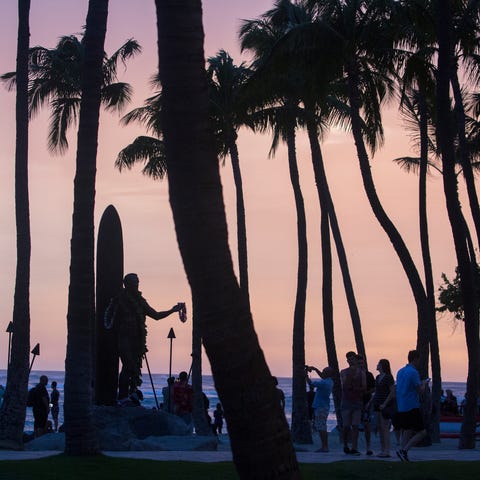 Tourists and locals watch the sunset near a statue